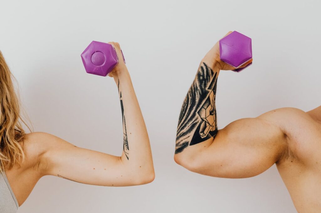 Two individuals flexing their muscles with purple dumbbells, showcasing tattoos and fitness dedication.